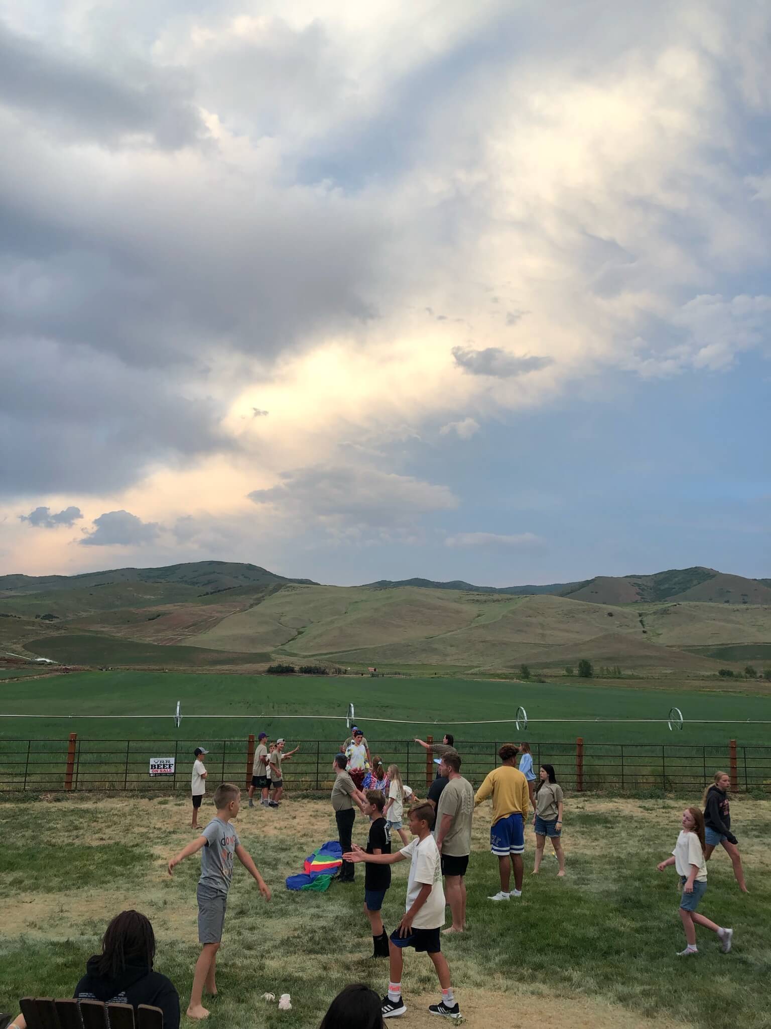 A photo of campers and counselors playing with a parachute with a cloudy backdrop.